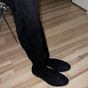 Svarta mockastövlar - Snygga svarta stövlar i mocka med en stilren design. De är knähöga och perfekta för höst och vinter. Stövlarna har en diskret snörning baktill och en platt sula för bekväm passform. Perfekta för både vardag och fest! Storleken 39. (Lite dammiga men tar självklart bort). Inte fri frakt.