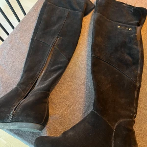 Svarta mockastövlar med dragkedja - Säljer ett par snygga svarta stövlar i mocka med dragkedja på sidan. Perfekta för höst och vinter, de är både stiliga och bekväma. Passar bra till både jeans och klänning. Använda men i mycket bra skick. Vagabond Overknee, går vika ner men ena stöveln har en reva som syns då. Jättebra skick förutom revan som ej syns om man använder dom som overknee