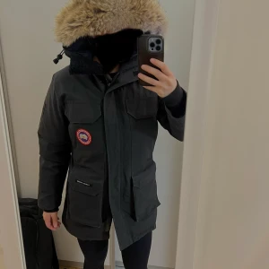 Svart parkajacka från Canada Goose - Säljer en svart parkajacka från Canada Goose i mycket bra skick. Jackan har en stor huva med päls och praktiska fickor framtill. Perfekt för kalla vinterdagar. Storlek xs