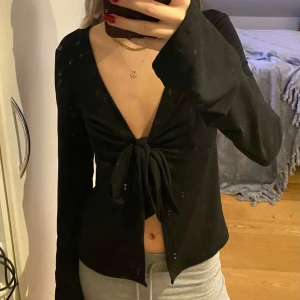Svart långärmad topp med knyt - Säljer en snygg svart långärmad topp med knyt framtill. Den har en djup v-ringning och är perfekt för både vardag och fest. Toppen är i bra skick och passar till många olika outfits. Perfekt för höst och vår!