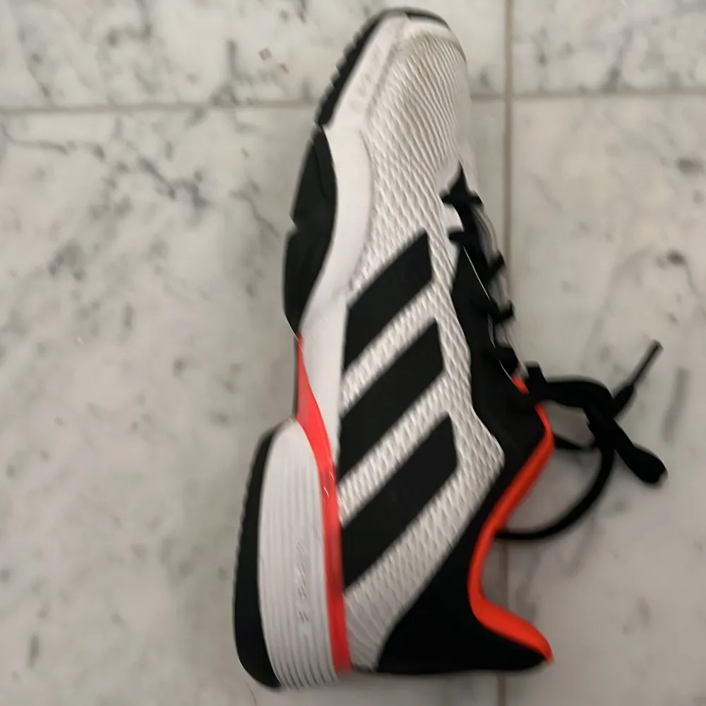 Säljer ett par Adidas sneakers i vitt och svart med coola röda detaljer. Skorna har en sportig design med snörning och är perfekta för träning eller vardagsbruk. De är i mycket bra skick och redo för nya äventyr!. Skor.