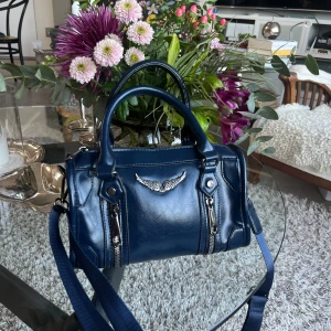 Mörkblå axelväska med silverdetaljer - Säljer en snygg mörkblå axelväska i skinn med coola silverdetaljer. Väskan har två dragkedjor framtill och en justerbar axelrem. Den är köpt i Grekland och inte äkta🫶