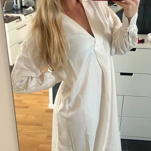 Vit långklänning - Säljer en elegant vit långklänning i ett mjukt och bekvämt material. Klänningen har långa ärmar och en v-ringad design som ger en stilren look. Perfekt för vår och sommar, både till vardags och festliga tillfällen.