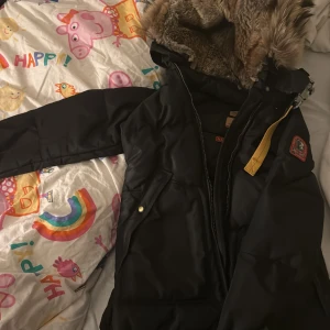 Svart vinterjacka med päls från Parajumpers - Säljer en svart vinterjacka från Parajumpers med pälsfodrad huva. Jackan har en dragkedja och en cool patch på ärmen. Perfekt för kalla vinterdagar! 🖤pris kan diskuteras vid snabb affär#parajumper#moncler# canada goose#colmar