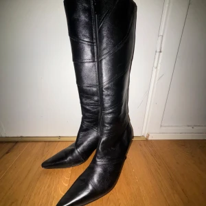 Svarta stövlar med spetsig tå Från MANNA(Italien) - Snygga svarta stövlar i skinn med spetsig tå och klack. Perfekta för höst och vinter, dessa boots har en elegant design som passar både till vardags och fest. De är i mycket bra skick och redo att ge din outfit en stilfull touch.En synlig defekt på höger spets där den är lite kantstött,perfekt för redo objekt eller för den okräsne går det att putsa upp dom! Osäker på storlek men 38-39 är storleken efter mätning.