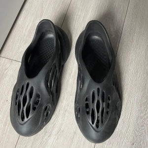 Yeezy - Säljer ett par svarta sneakers i mycket bra skick. De har en unik, futuristisk design med hålmönster och en vågig sula. Perfekta för en cool och avslappnad stil. Passar bra till både vardags och som statement piece. Storlek e lite knasigt för fick dem av min kusin men dem passar mig har 43/44 a kopie
