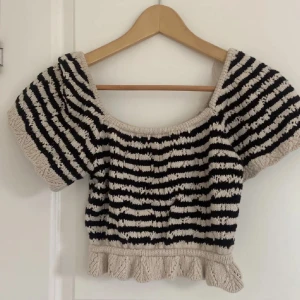 Randig croppad topp - Säljer en superfin randig topp i svart och beige. Den är croppad och har korta ärmar med en söt volangdetalj längst ner. Perfekt för sommardagar eller en avslappnad fest. Toppen är i mycket bra skick och passar perfekt till ett par jeans eller kjol. 
