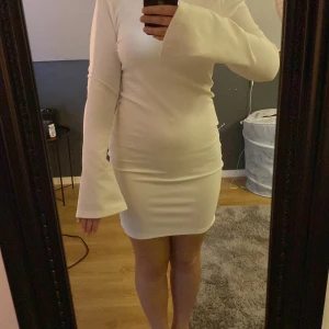 Vit klänning med snörning - Säljer en superfin vit klänning med lång ärm och snörning i ryggen. Den är tight och kort. Materialet känns mjukt och stretchigt, vilket gör den bekväm att bära hela kvällen. Passar perfekt till både sommar och vår!