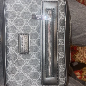 Gucci axelväska i grått mönster - Säljer en snygg Gucci axelväska i grått med det klassiska GG-mönstret. Väskan har en dragkedja framtill och är i mycket bra skick. Perfekt för både vardag och fest! Kommer med originalpåse.