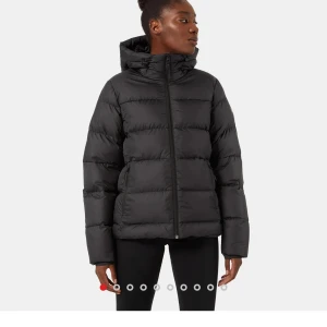 Svart pufferjacka med huva - Säljer en svart pufferjacka i mycket bra skick. Den är perfekt för vintern med sin varma vaddering och praktiska huva. Jackan har en dragkedja framtill och långa ärmar. Den är både stilren och funktionell, idealisk för kalla dagar.