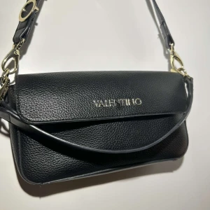 Svart axelväska från Valentino - Snygg svart axelväska från Valentino i skinn. Väskan har en justerbar axelrem med gulddetaljer och Valentino-logga. Perfekt för både vardag och fest! 🖤