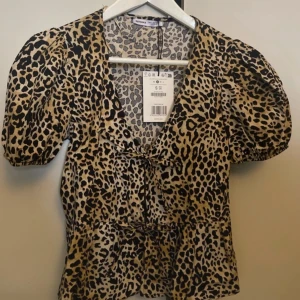 Leopardmönstrad blus med knyt - Snygg leopardmönstrad blus från  Bershka storlek s . Blusen har korta puffärmar och en v-ringad design med knyt framtill. Perfekt för en trendig look både till vardags och fest. 🐆✨
