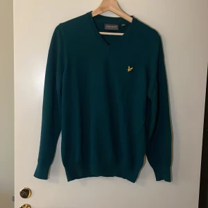 Grön tröja från Lyle & Scott - Säljer en snygg grön tröja från Lyle & Scott i mycket bra skick. Den har en v-ringad design och ett litet broderat emblem på bröstet. Perfekt för både vardag och lite finare tillfällen. Passar bra till höst och vår! Pris går alltid att förhandlas!