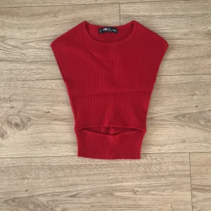 Röd ribbad topp - Säljer en snygg röd ribbad topp i storlek XXS. Perfekt för lager-på-lager eller som ett statement-plagg. Den är ärmlös och har en tight passform som framhäver figuren. Den har en slit vid magen som visar magen vilket är jätte snyggt och trendigt. Toppen är i mycket bra skick och redo för nya äventyr! 