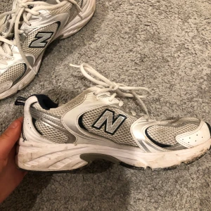 Vita New Balance sneakers - Säljer ett par vita New Balance sneakers i bra skick. De har en klassisk design med snörning och är perfekta för vardagsbruk. Skorna har en bekväm passform och är gjorda i syntetmaterial med meshdetaljer för extra andningsförmåga.