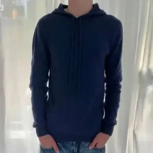 Mörkblå hoodie från John Henric - Säljer en supermjuk och lyxig mörkblå hoodie från John Henric, gjord i 100% kashmir. Perfekt för kyliga dagar med sin varma och bekväma passform. Den har långa ärmar och en klassisk huva med dragsko. Passar både till vardags och mysiga hemmakvällar.