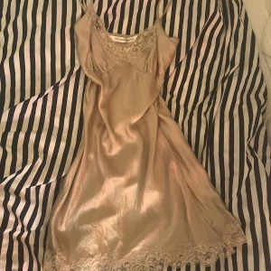 Champagnefärgad nattlinne från Victoria's Secret - Säljer en elegant champagnefärgad sidenklänning från Victoria's Secret. Den har vackra spetsdetaljer vid halsringningen och längs nederkanten. Perfekt för en lyxig kväll eller som en fin underklänning. Klänningen har smala axelband och en mjuk, glansig finish.