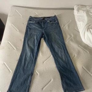 Blå jeans med broderade bakfickor - Säljer ett par snygga blå jeans med unika broderade detaljer på bakfickorna. De har en bootcut-stil och är perfekta för en avslappnad look. Jeansen har en fläck som knappast syns. Midjemått: 43cm Innerbenslängd: 79cm skickar inga bilder på !