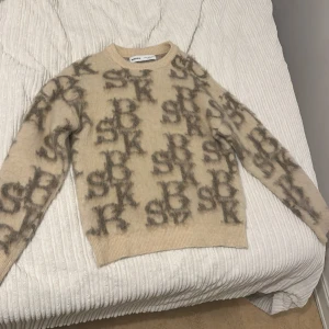 Beige mönstrad tröja från Bershka - Säljer en supermjuk och stilren beige tröja från Bershka. Den har ett coolt mönster med bokstäver i en mörkare nyans. Perfekt för att hålla sig varm och snygg under hösten och vintern. Tröjan har långa ärmar och en bekväm passform. Väldigt bekvämt att ha på sig. 🧡😍