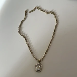 Guldplätterat halsband med hänge - Snyggt guldhalsband med en rektangulär hängsmycke dekorerad med små stenar. Perfekt för att ge en elegant touch till din outfit. Kedjan är i en klassisk stil och hängsmycket har en glittrig look. Passar både till vardags och festliga tillfällen.