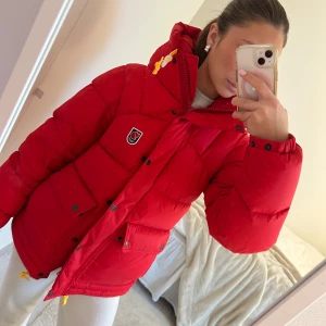 Röd dunjacka från Fjällräven - Säljer en supervarm och snygg röd dunjacka från Fjällräven. Perfekt för kalla vinterdagar med sin tjocka vaddering och mysiga huva. Jackan har praktiska fickor och stängs med både dragkedja och knappar. Den är i mycket bra skick och redo för nya äventyr! 🔥