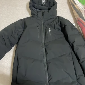 Svart dunjacka från Sail Racing - Säljer en svart dunjacka från Sail Racing i mycket bra skick. Jackan är perfekt för kalla vinterdagar med sin 500 fill power dunisolering. Den har en dragkedja framtill och en praktisk huva. Designad i Sverige och tillverkad i Vietnam. Perfekt för dig som vill hålla stilen i vinter! ❄️ sail racing 10/10