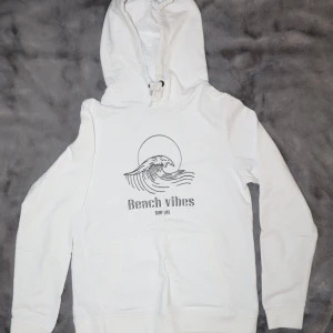 Vit hoodie med tryck 'Beach Vibes' - Vit hoodie med trycket 'Beach Vibes' och en  vågdesign. Den har en justerbar huva med snören. Den är i bra skick!