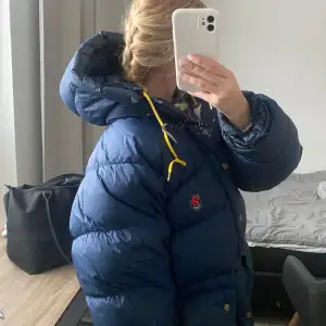 Säljer en mörkblå dunjacka från Fjällräven i bra skick. Perfekt för kalla vinterdagar. Den har en snygg och klassisk design med Fjällrävens logga på bröstet. Storlek M