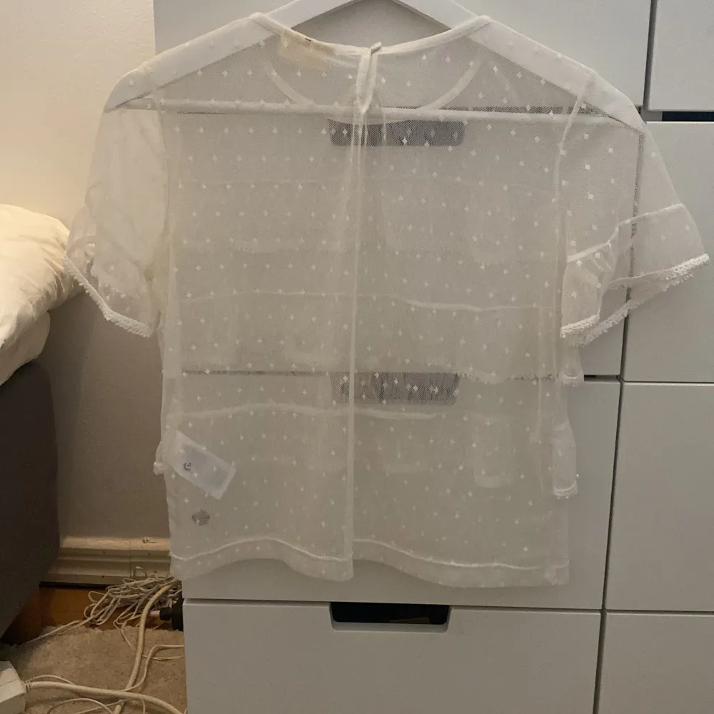 Säljer en superfin vit transparent topp med korta ärmar och flera lager volanger. Toppen har ett prickigt mönster och är perfekt för sommarens fester. Den är i mycket bra skick och ger en luftig och stilren look. Passar perfekt över ett linne eller en snygg bh.. Toppar.