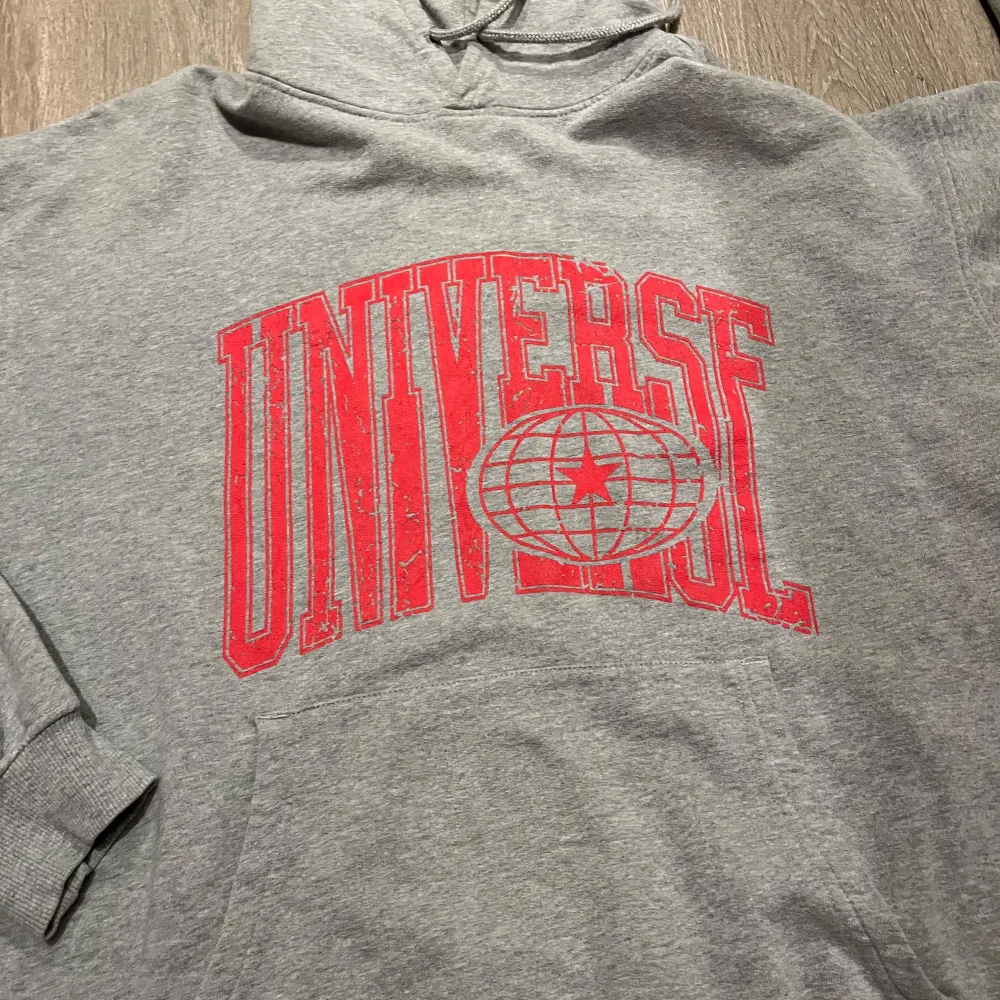 Säljer en grå hoodie från Vailent i storlek L. Den har en stor röd text 'UNIVERSE' på framsidan och en bekväm passform. Perfekt för höst och vinter med sin mysiga huva och långa ärmar. Använd fåtal gånger. Tröjor & Koftor.