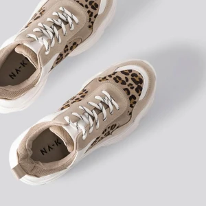Beige sneakers med leopardmönster från NA-KD - Snygga sneakers i beige med leopardmönster. De har en chunky vit sula och snörning framtill. Skorna är oanvända. 