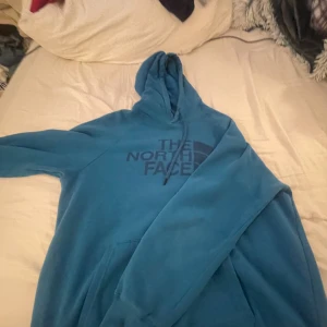 Blå hoodie från The North Face - Säljer en snygg blå hoodie från The North Face i mycket bra skick. Den är perfekt för kyliga dagar med sin mjuka insida och klassiska logga på bröstet. Passar både till vardags och för utomhusaktiviteter. Huvan har dragsko för justerbar passform.