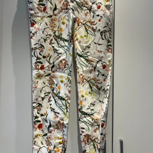 Byxor Zara M - Vita byxor med blommigt mönster. Byxorna har en smal passform och är tillverkade i ett tunt, lätt material. De har två fickor framtill och två fickor baktill. Capri Längd