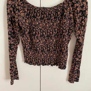 Blommig långärmad topp - Säljer en superfin svart topp med små blommor i rosa. Den är långärmad och har en tight passform med en smockad effekt. Perfekt för både vardag och fest! Storlek S. Endast använd fåtal gånger💗