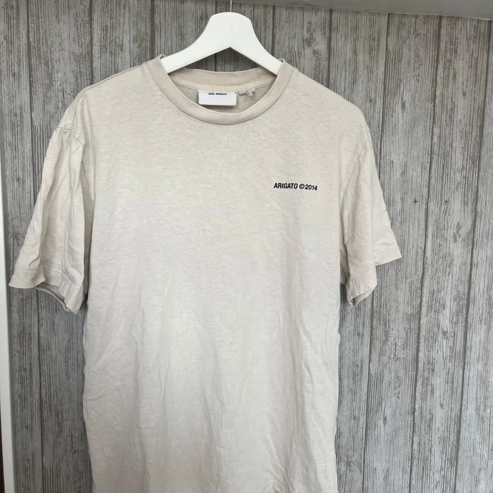 Beige t-shirt från Arigato i bra skick. Köpt på NK så äkta. Storlek L men passar som M/L. T-shirts.