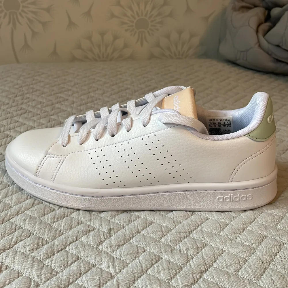 Säljer ett par nya snygga, supersköna vita Adidas Advantage sneakers.  Mycket skön sula - cloudfoam.  Skorna har en stilren design med snörning och en diskret grön detalj på hälen. Säljes pga felköp.. Skor.