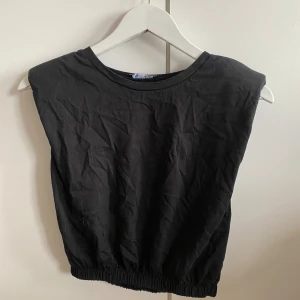 Svart ärmlös topp - Säljer en enkel och stilren svart ärmlös topp. Den har en elastisk nederkant som ger en bekväm passform. Perfekt för både vardag och fest!