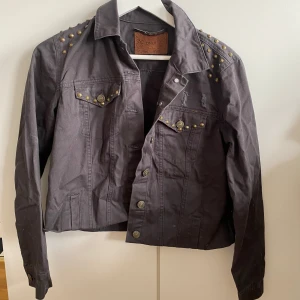 Svart jacka med nitar och tryck - Säljer en cool svart jacka från Only med nitar på axlarna och ett stort tryck på ryggen som säger 'IT'S ALL GOOD'. Jackan har en klassisk krage och knappar framtill. Perfekt för en avslappnad och edgy stil!