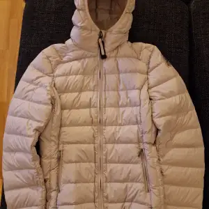 Säljer en superlätt och varm beige dunjacka från Parajumpers. Jackan har en dragkedja framtill och en mysig huva för extra skydd mot kylan. Perfekt för ungdom. Den är i storlek Y/L och i bra skick. Finns dock en synlig fläck.