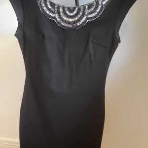 Svart kort klänning  - Svart kort klänning som sitter tajt och är längden lite över knät Den är ca 65 cm lång. Använd endast en gång mycket bra skick  Paletter på framsidan och ryggen är öppen.