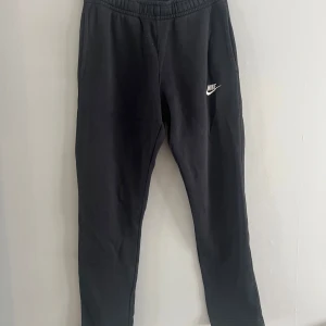 Svarta mjukisbyxor från Nike - Säljer ett par svarta mjukisbyxor från Nike i storlek S. De är superbekväma och perfekta för chill dagar eller träning. Byxorna har en elastisk midja och en liten Nike-logga på benet. De är i bra skick och redo för nya äventyr!
