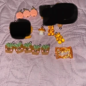 Söta örhängen och berlocker - Säljer ett gäng supersöta örhängen och berlocker! Det finns örhängen som ser ut som persikor i en härlig orange färg. Berlockerna inkluderar en svamp, en björn, små krukor med växter och en godisbit med texten 'Sweet'. Perfekta accessoarer för att ge din outfit en lekfull touch!