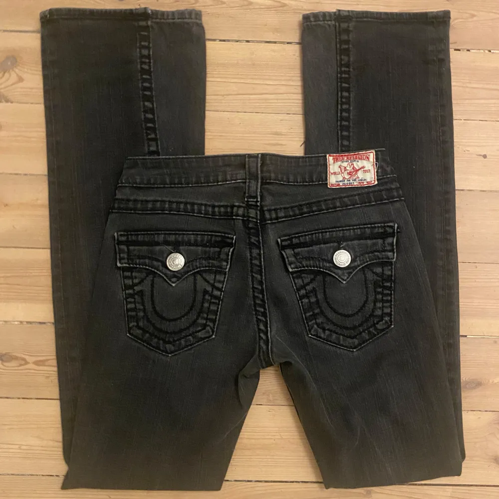 Säljer ett par snygga utsvävngda svarta jeans från True Religion. De har en cool design med tydliga sömmar och knappar i silver. Jeansen är i bra skick och har en klassisk femficksmodell. Perfekta för både vardag och fest! . Jeans & Byxor.