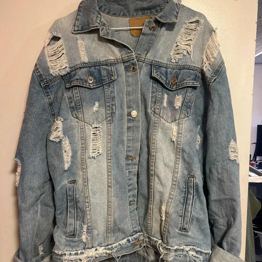 Säljer en cool och trendig ljusblå jeansjacka med slitna detaljer. Jackan har en klassisk krage och knappar framtill. Perfekt för en avslappnad stil och passar bra till både vår och höst. Den har långa ärmar och en fransig nederkant som ger en extra edge.. Takit.