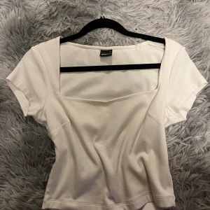 Vit kortärmad topp - Säljer en stilren vit topp från Gina Tricot. Den har använts extremt lite och är i nytt skick. Den har korta ärmar och en fyrkantig halsringning som ger en modern touch. Perfekt för både vardag och fest!