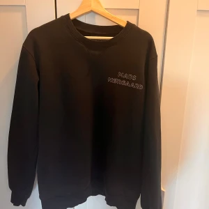 Svart sweatshirt från Mads Nørgaard - Snygg svart sweatshirt från Mads Nørgaard med broderad logga på bröstet. Tröjan har långa ärmar och ribbade muddar vid ärmslut och nederkant. Perfekt för en stilren look.