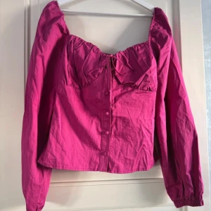 Rosa topp med prislapp - Säljer tjusig rosa blus med både knappar och knytning över bysten. Aldrig använd.  Prislapp sitter kvar. Ordinariepris 499kr. Storlek 40
