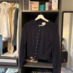 Mörkblå kofta från H&M - Säljer en stilren mörkblå kofta från H&M med knappar framtill. Perfekt för att hålla sig varm och snygg under kyligare dagar. Koftan har långa ärmar och en klassisk rund halsringning. Nästan aldrig använd och köpt för 199 tror jag 
