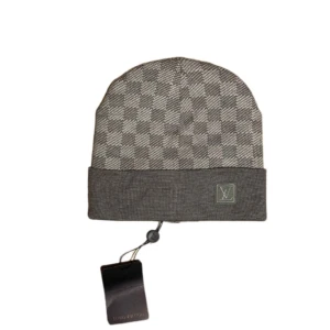 Grå rutig mössa  - Snygg grå mössa med klassiskt rutigt mönster. Mössan har en uppvikt kant med en diskret logotyp. Perfekt för att hålla stilen under kallare dagar.