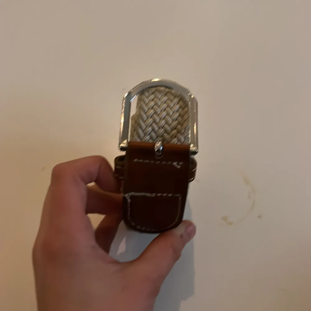 Säljer ett snyggt beige flätat bälte med ett stilrent silverfärgat spänne. Perfekt för att ge en extra touch till din outfit. Bältet har bruna detaljer vid spännet som ger en fin kontrast.100cm långt bälte. Muu.